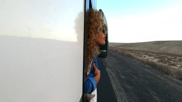 beautiful caucasian young woman travel outside the camper van with wind in the curly hair travel