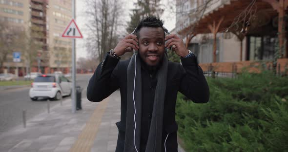 African Man Puts on Headphone Walking in a City