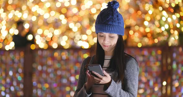Woman look at mobile phone over christmas light decoration