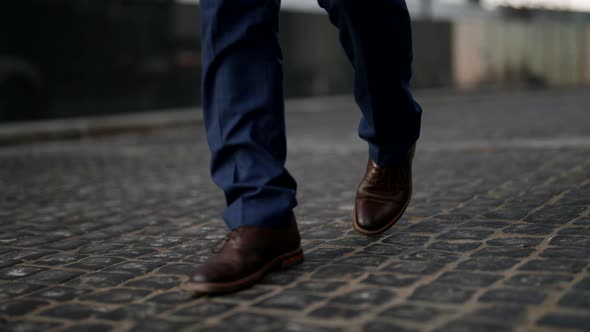 Men's Feet in Blue Plaid Trousers and Brown Shoes Walk on the Cobblestones