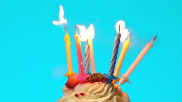 A Piece of Birthday Cake with Burning Candles on a Blue Background is Blown Out