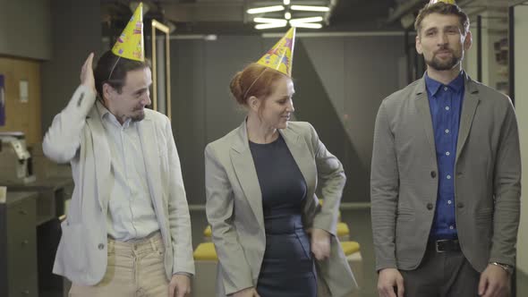 Cheerful Caucasian Redhead Woman Standing with Two Male Colleagues in Open Space Office and Looking