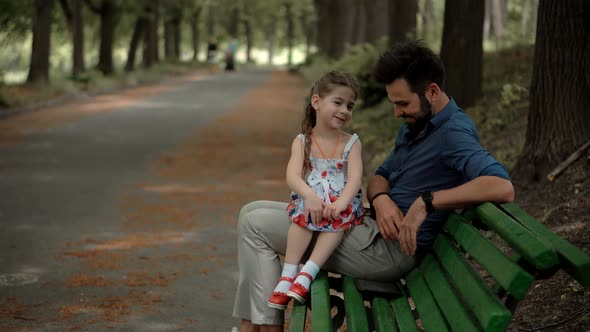 Happy Beautiful Family Relaxing Together In Park. Daughter With Father Sitting On Bench.
