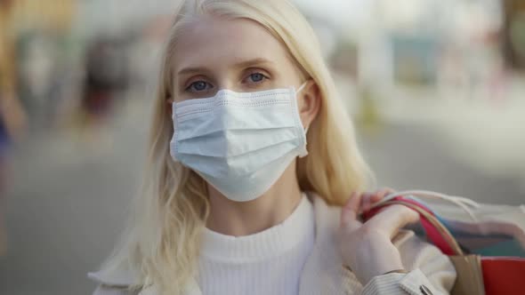 A Woman in a Medical Mask Holds Packages From Different Boutiques Behind Her Back Walks Forward and