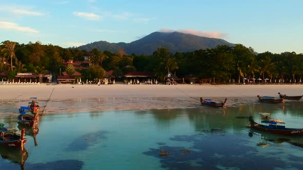 An aerial shot of a white sand beach with boat and green forest in the background.