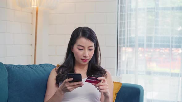 Young smiling Asian woman using smartphone buying online shopping by credit card.