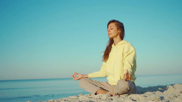 Beautiful Girl in Yellow Hoodie Doing Yoga on Beautiful Calm Sea Beach at Sunrise