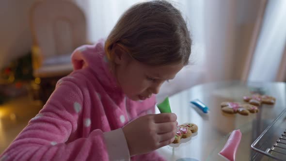 Charming Joyful Girl Decorating Christmas Cookie Gesturing Thumb Up Smiling Looking at Camera