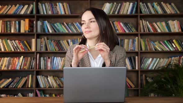 Thoughtful Brunette in Jacket Over White Blouse Holds Pen