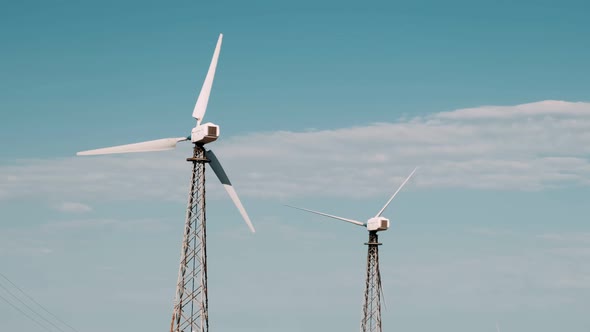 Slow motion of the blades of a large wind turbine in a field against a blue sky. Windy park.