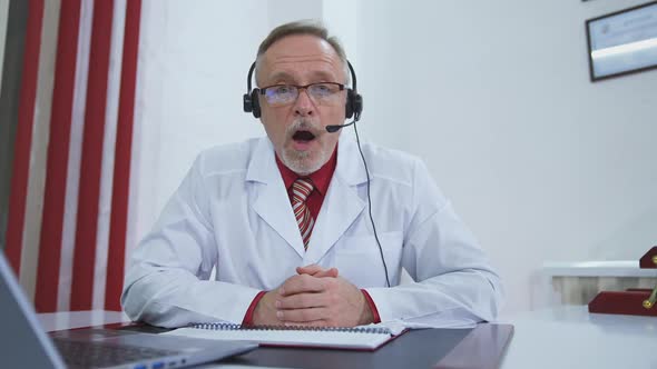 Doctor working on line with laptop. Senior doctor having video chat with patient on laptop