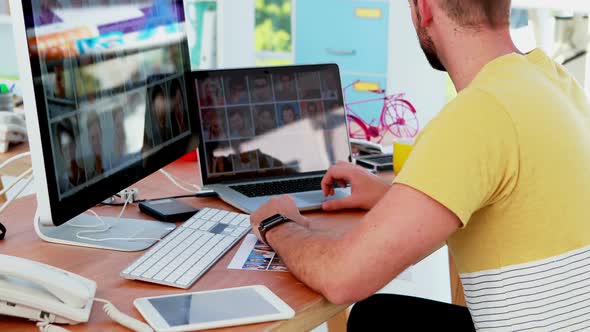 Male executive looking photos on laptop and computer at desk 4k