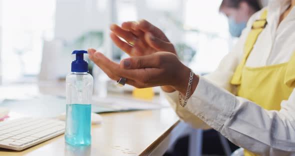 Mid section of woman sanitizing her hands at office