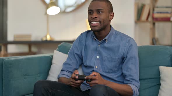 Young African Man Playing Video Game on Sofa