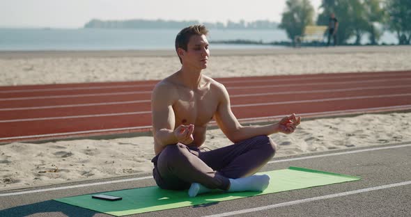 Young Sporty Man Sitting in Lotus Pose Meditating Outside
