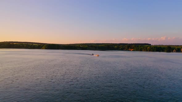 Beautiful evening landscape over the water. Motor boat floating at orange sunset.