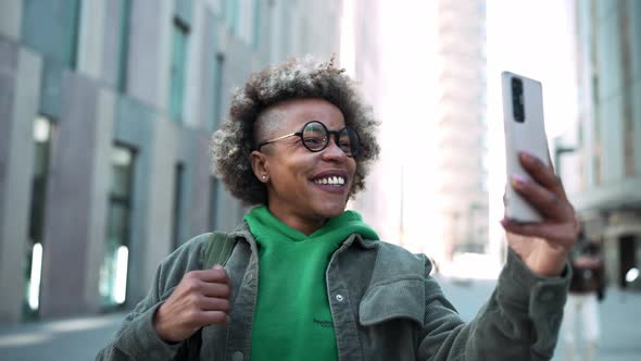 Smiling adult African woman wearing casual clothes talking by video call on phone