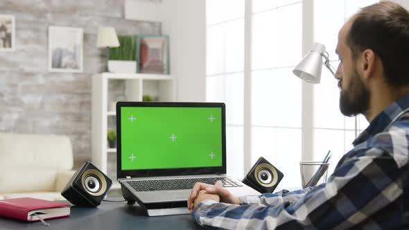 Over the Shoulder Zoom in Shot of Man Looking at Laptop with Green Screen