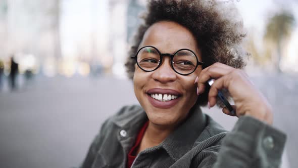 Smiling adult African woman wearing casual clothes talking by mobile