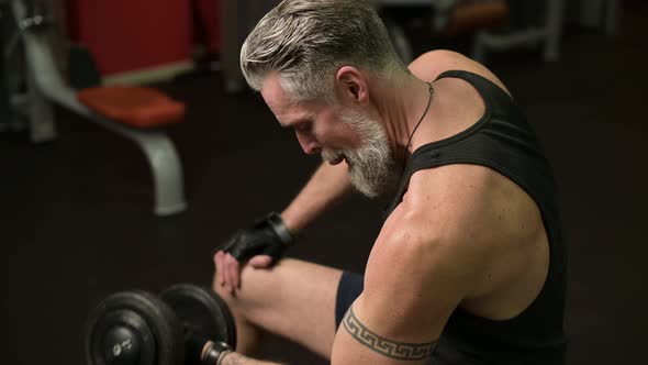 Close-up of a gray-haired bodybuilder in the gym. Gray-haired man pumping biceps