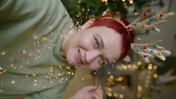 Cheerful adult woman in reindeer horns makes Christmas selfie on smartphone