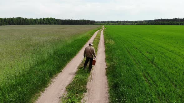 Lonely Lost and Disappointed Man Walking Alone in Despair with Suitcase By Country Road in a Green