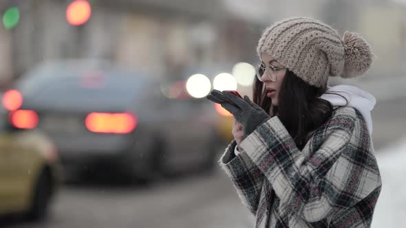 A Beautiful Young Darkhaired Woman in Round Glasses and a Plaid Coat Walks Around the City on a