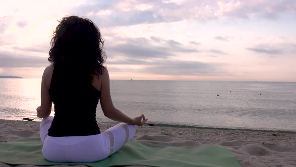 Woman relaxing in lotus pose on the beach. Meditation near the sea at sunrise.