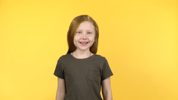 Red-haired Child Smiling Shyly and Looking at the Camera on Yellow Background