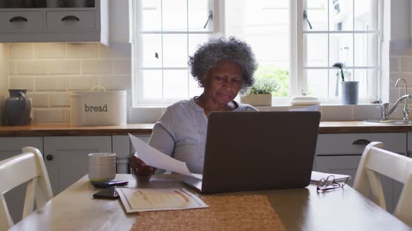 Stressed senior african american woman using laptop and calculating finances at home