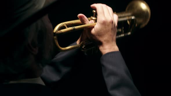 Confident Musician in Hat Plays Musical Trumpet Pressing Valves in Studio Closeup on Black