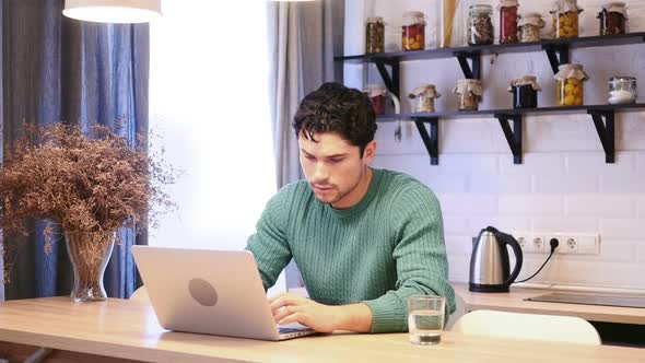 Man Busy Working on Laptop While Sitting in Kitchen