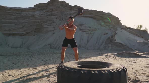 Muscle Athlete Strongman Man Hits a Hammer on a Huge Wheel in the Sandy Mountains in Slow Motion