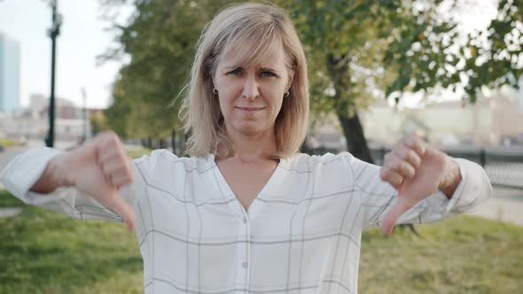 Portrait of Disappointed Woman Showing Thumbsdown Gesture with Both Hands Standing Outdoors