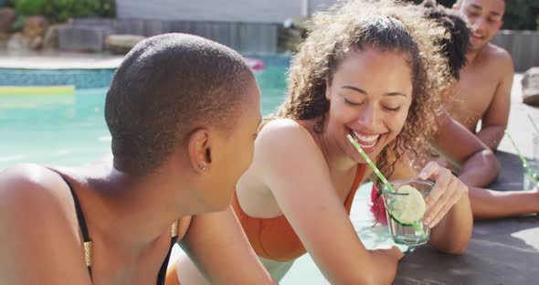 Two happy female friends having drinks laughing in pool