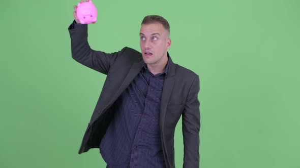 Stressed Businessman in Suit Holding Piggy Bank and Giving Thumbs Down