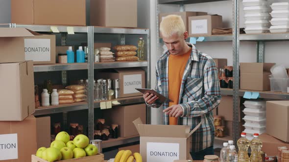 Man Using Digital Tablet While Packing Donation Boxes