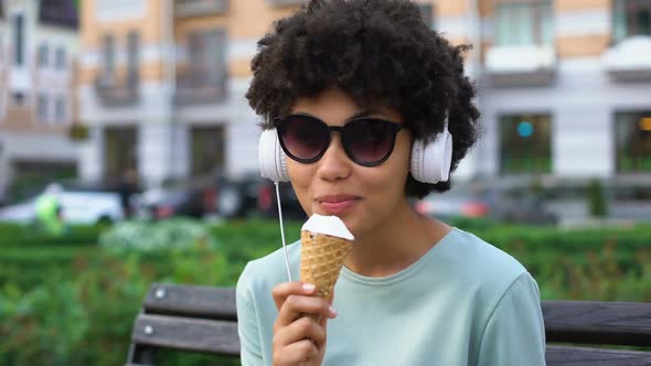 Creative Carefree Woman Enjoying Music in Headphones, Eating Ice-Cream on Bench