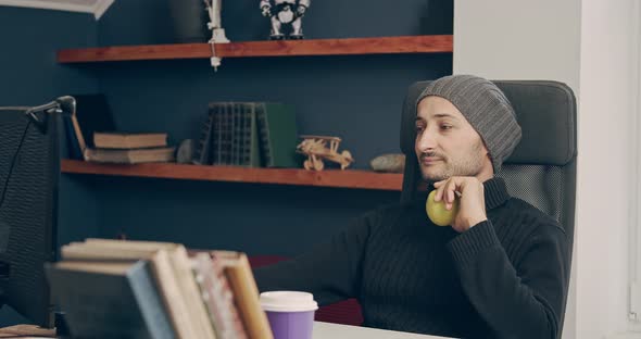 A Man is Working at Home on a Computer and is About to Eat an Apple