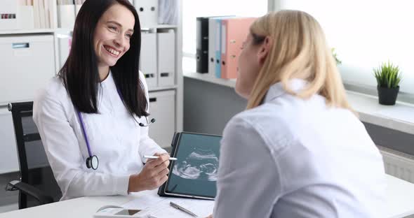 Smiling Gynecologist and Happy Patient Watching an Ultrasound Scan of Child on Tablet