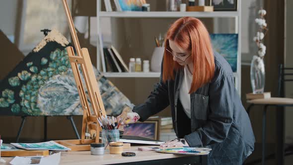 Inspired Busy Focused Redhead Girl Artist Woman Painter in Art Studio Background Paints with Wide