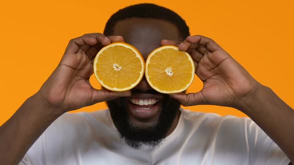 Playful African Male Holding Orange Slices Front Eyes, Vitamin Nutrition, Health