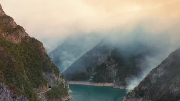 Thick white smoke from a fire covering sky. Fog rising over water and hills in the morning.