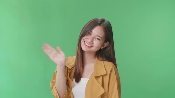 Happy Asian Woman Waving Hands And Looking At Camera In The Green Screen Studio