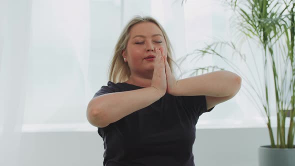 Blonde Overweight Smiling Woman Meditating on Yoga Mat in White Modern Studio