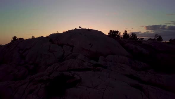 Fly over Inukshuk on Rocky Pine Tree Island at Sunset, Drone Aerial Wide Dolly In. View of Blue Lake