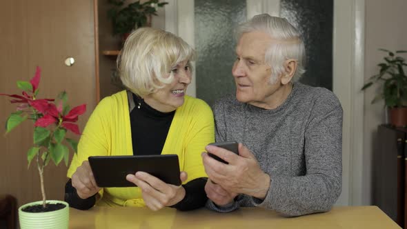 Pretty Mature Senior Couple Grandparents Enjoy Online Shopping on Phone, Tablet