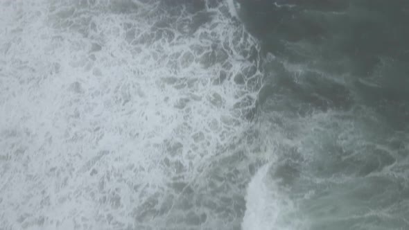 White waves crash against a rocky jagged fog shrouded coastline, aerial reveal