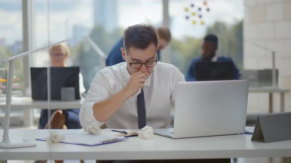 Unhealthy Male Employee Sneezing While Working in Workplace in Office