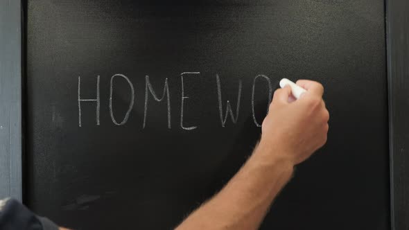 Male hands writing words HomeWork with chalk on blackboard. Education concept